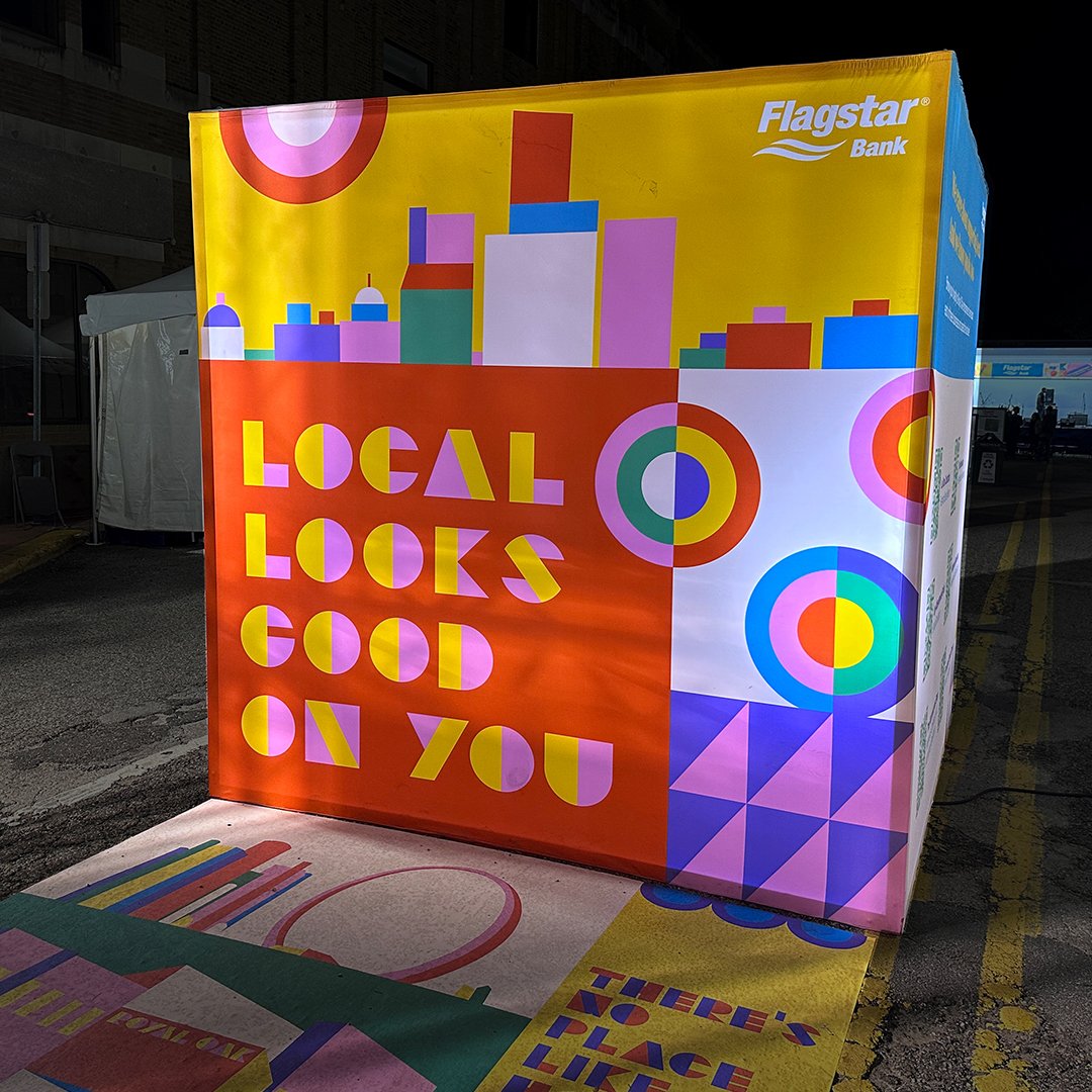 A photograph of a dimensional cube installation at an event with colorful geometric illustration wrapped around it.